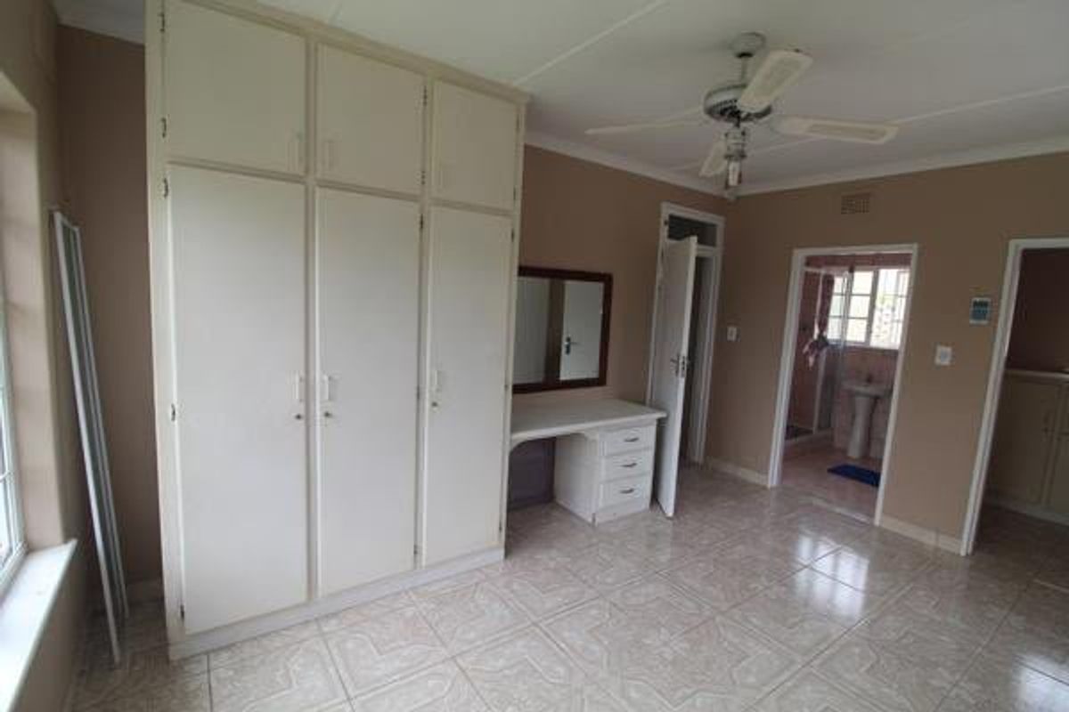 Spacious bedroom featuring built-in cupboards, a vanity unit, ceiling fan, and tiled flooring, with direct access to an en-suite bathroom.