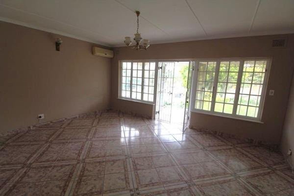 Spacious, empty living area featuring tiled flooring, a split-system air conditioner, and large multi-pane windows providing natural light and garden access.