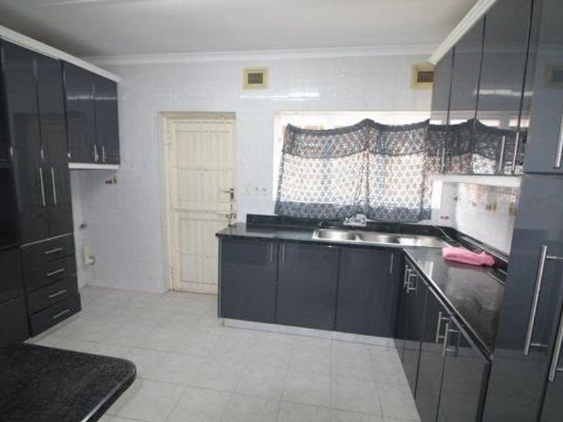 A functional kitchen featuring dark high-gloss cabinetry, a double basin sink, tiled flooring, and a secure exterior door.