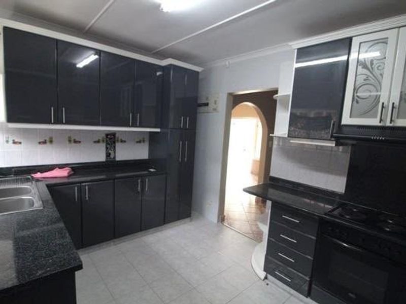 A functional kitchen featuring modern dark cabinetry, granite countertops, a double basin sink, and integrated cooking appliances with tiled flooring.