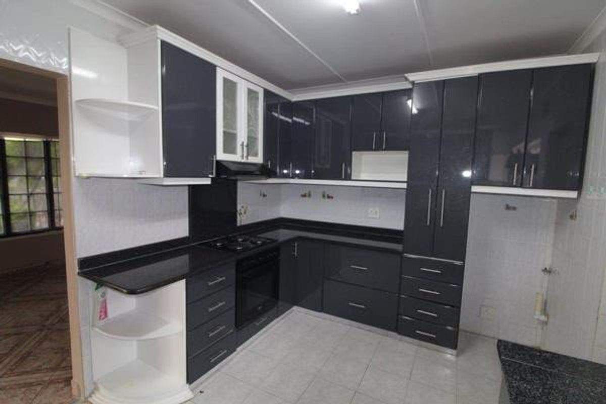 Modern kitchen featuring high-gloss dark cabinetry, contrasting white shelving, black granite countertops, and integrated cooking appliances with neutral tiled flooring.