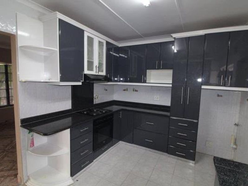 Modern kitchen featuring high-gloss dark cabinetry, contrasting white shelving, black granite countertops, and integrated cooking appliances with neutral tiled flooring.
