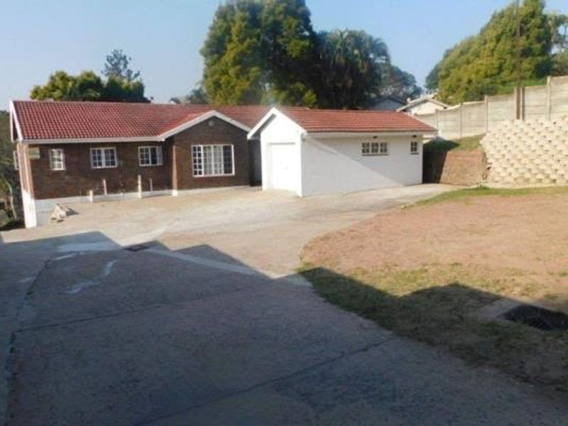 Front view of a brick house featuring a tiled roof, attached garage, and a large concrete driveway with an adjacent sloped yard area.