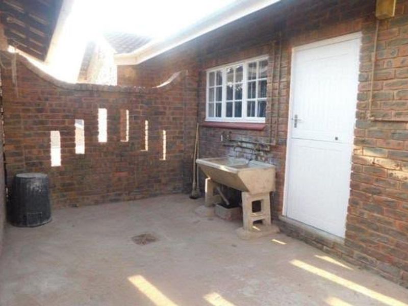 An outdoor laundry area featuring a concrete utility trough, exposed brick walls, and a secure access door.