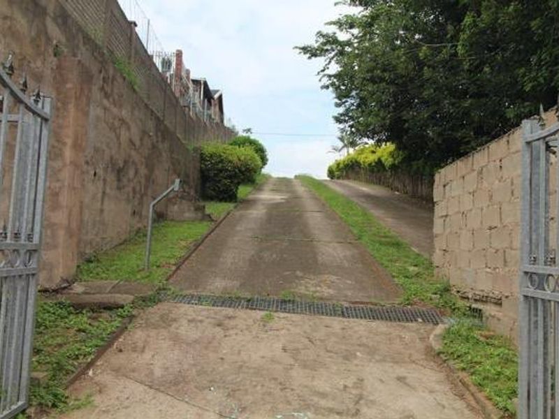 A steep concrete driveway leading up to the property, featuring metal security gates, retaining walls, and drainage infrastructure.