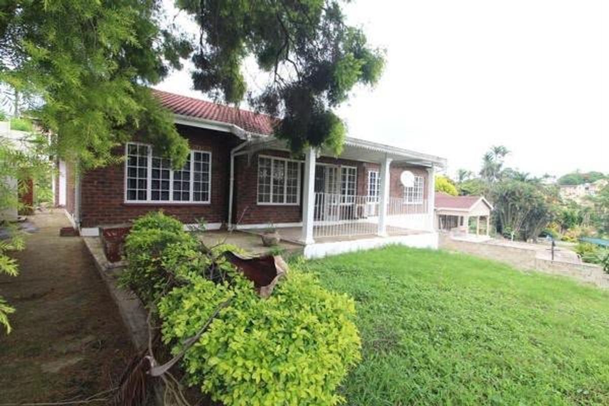 Rear view of a brick house featuring a covered patio, tiled roof, and a spacious garden area.