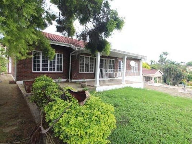 Rear view of a brick house featuring a covered patio, tiled roof, and a spacious garden area.