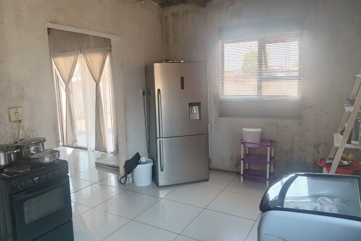Kitchen area featuring tiled flooring and a window with blinds, currently requiring significant wall finishing and maintenance to improve the overall condition.