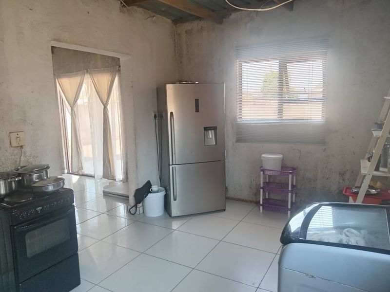 Kitchen area featuring tiled flooring and a window with blinds, currently requiring significant wall finishing and maintenance to improve the overall condition.