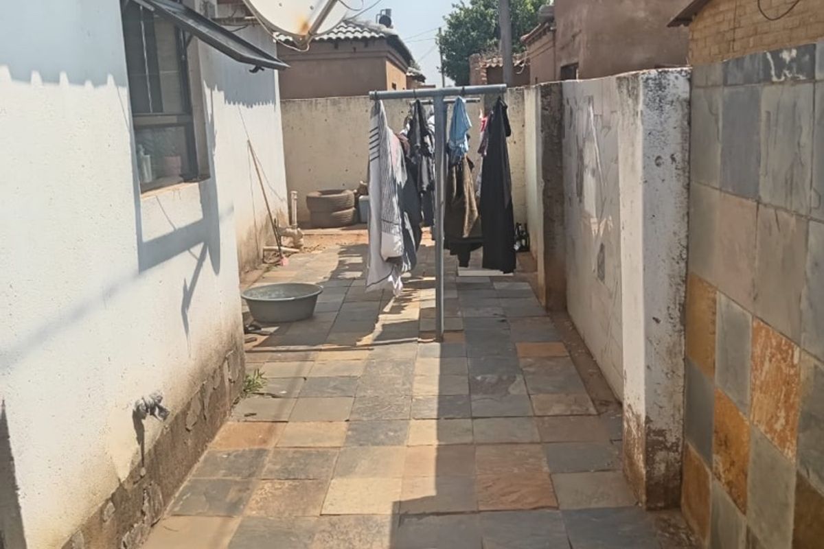 A narrow rear exterior walkway featuring slate tile paving, boundary walls, and an external tap, showing signs of wear and weathering.