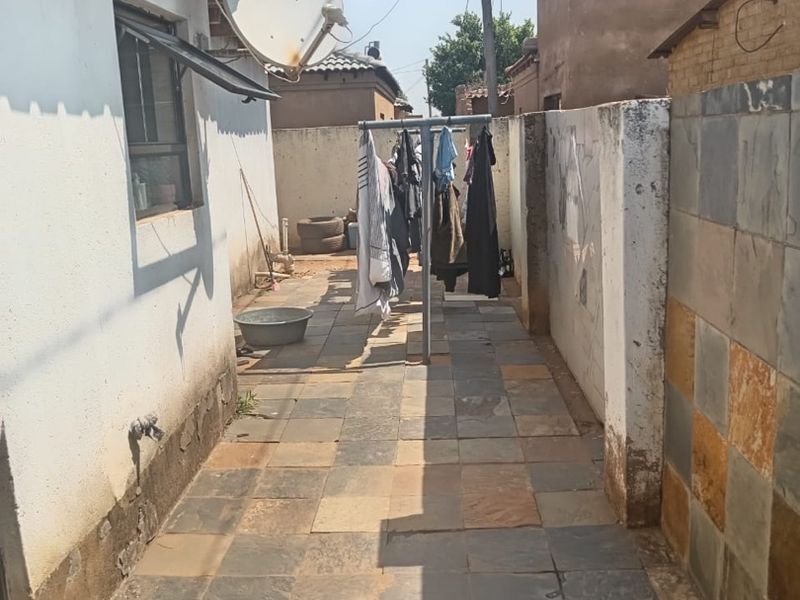 A narrow rear exterior walkway featuring slate tile paving, boundary walls, and an external tap, showing signs of wear and weathering.