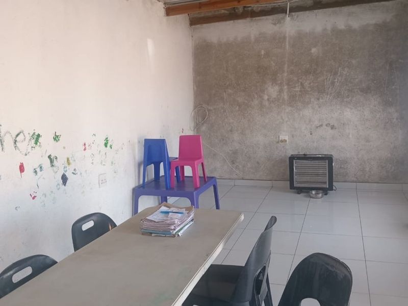 An interior living space featuring exposed timber roof beams, corrugated metal ceiling, and tiled flooring, currently requiring wall finishing and maintenance.