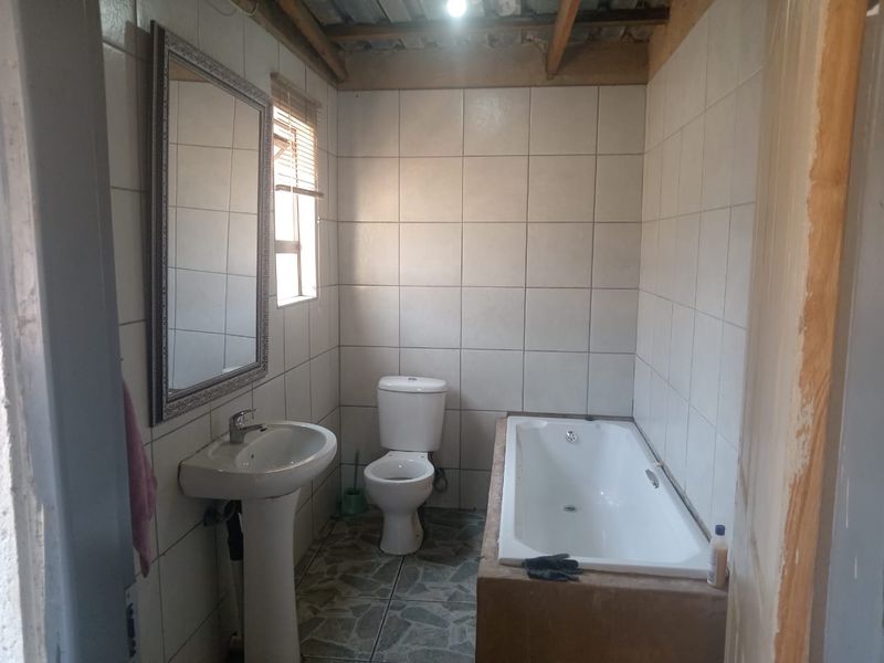 A functional bathroom featuring a pedestal basin, toilet, and built-in bathtub with tiled finishes, requiring some cosmetic finishing to the ceiling and door frame.