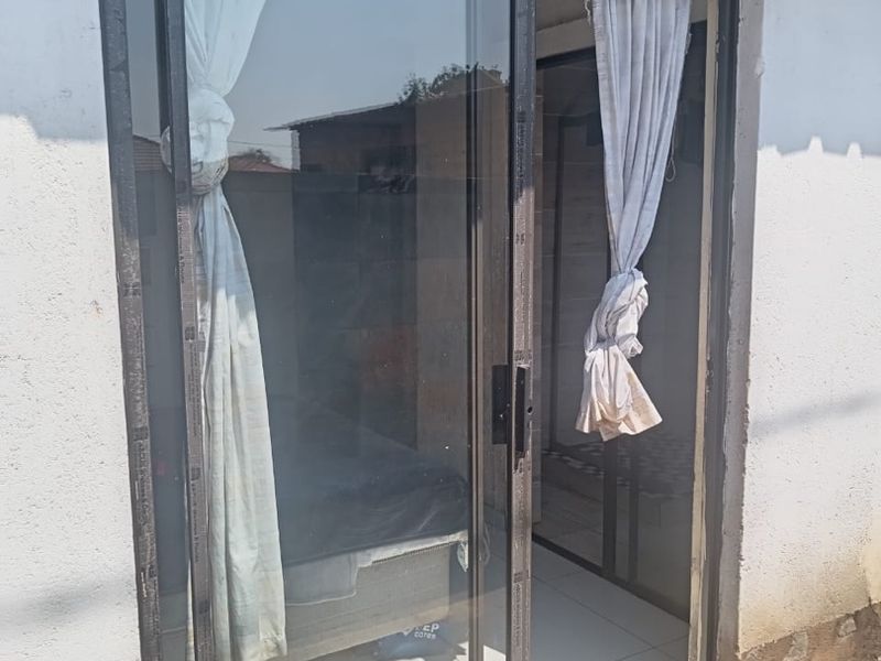 Exterior view of a rear sliding glass door entrance featuring tiled flooring and an exterior wall light fixture.