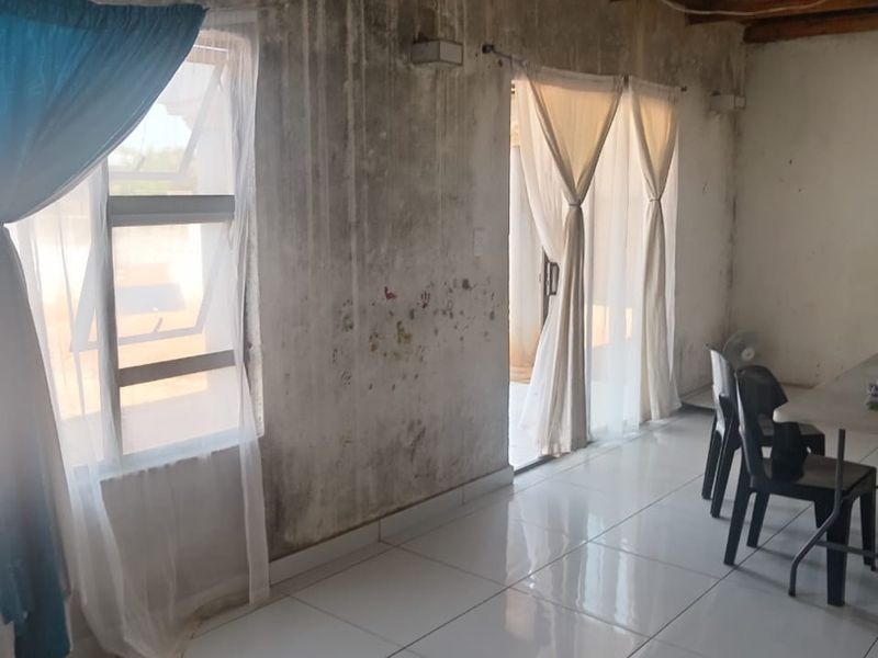 Living area featuring tiled flooring and exposed timber rafters, currently showing significant wall staining and signs of damp damage requiring maintenance.
