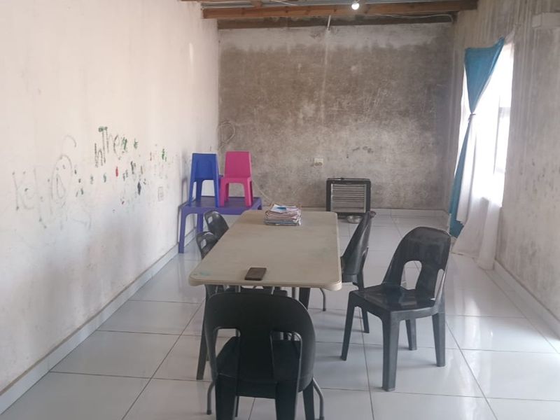 A living area featuring ceramic floor tiles and exposed timber ceiling beams, currently requiring significant wall repairs and cosmetic finishing.