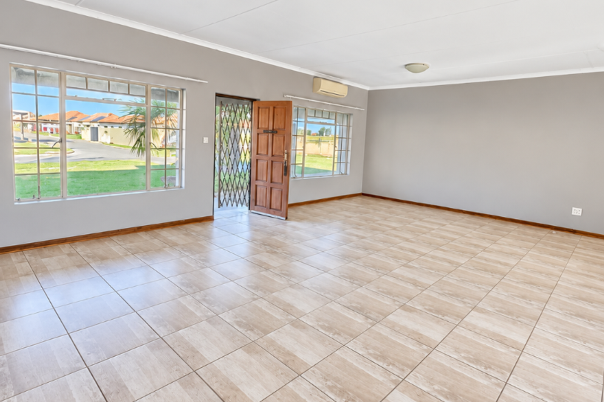 Spacious, light-filled living area featuring neutral tiled flooring, air conditioning, and large windows providing ample natural light and exterior views.