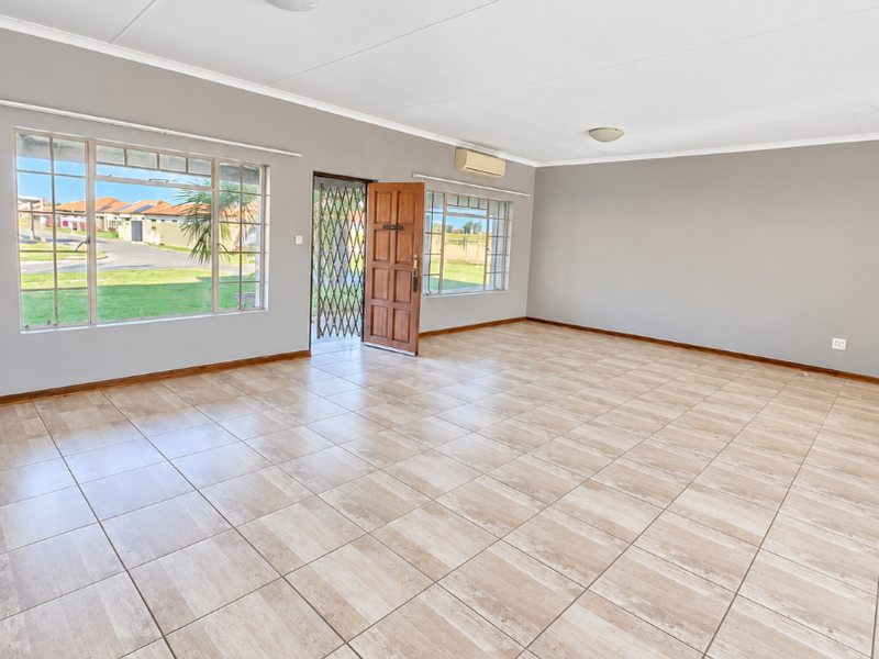Spacious, light-filled living area featuring neutral tiled flooring, air conditioning, and large windows providing ample natural light and exterior views.