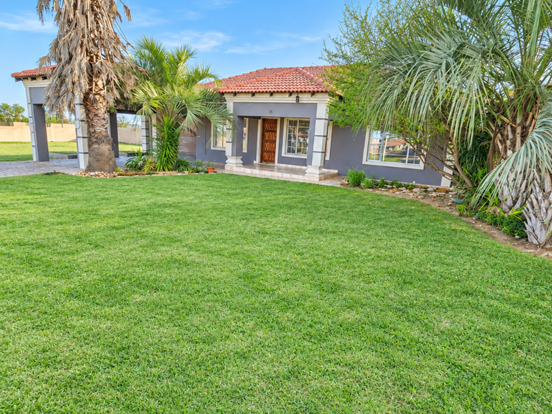 A well-maintained single-story house featuring a terracotta tiled roof, covered entrance porch, and a spacious, manicured front lawn with established landscaping.