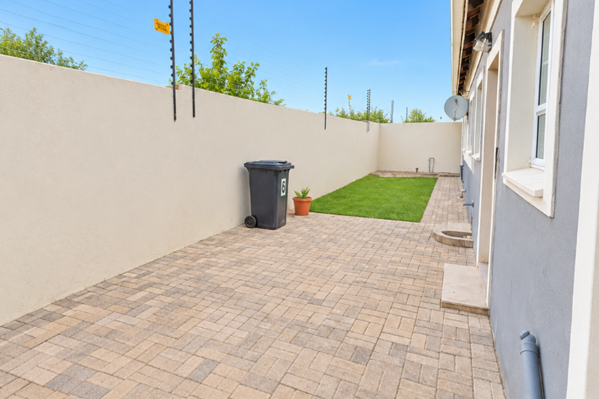 A neat rear courtyard featuring paved flooring, a small lawn area, and secure boundary walls with electric fencing.