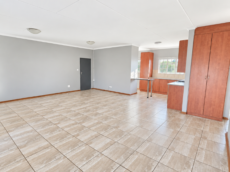 Spacious open-plan living area featuring neutral grey walls, tiled flooring, and a functional kitchen with built-in cabinetry and ample storage space.