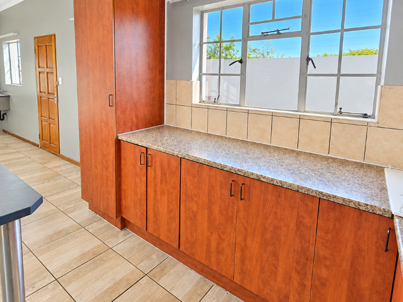 A functional kitchen area featuring wood-look cabinetry, tiled backsplash, and ceramic flooring, offering a clean and neutral space ready for updates.