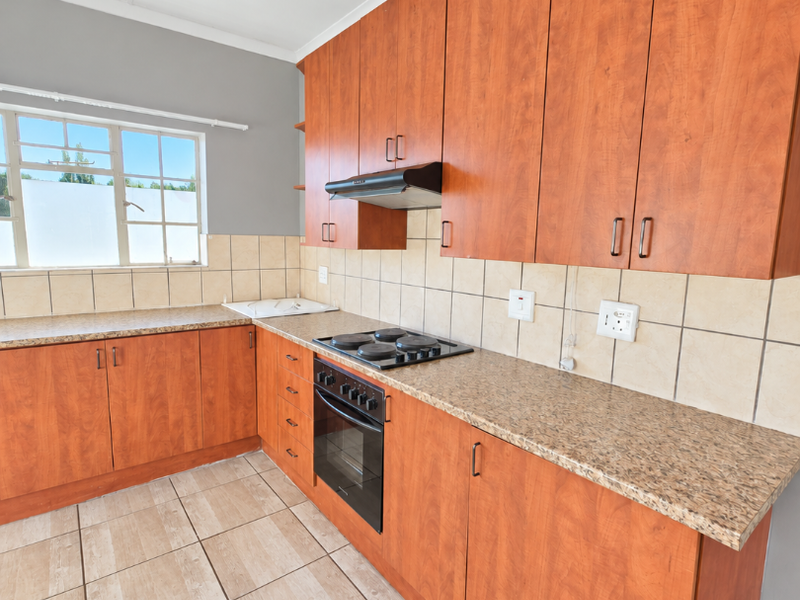 A functional kitchen featuring wood-look laminate cabinetry, granite-effect countertops, built-in oven with hob, and neutral ceramic floor tiling.