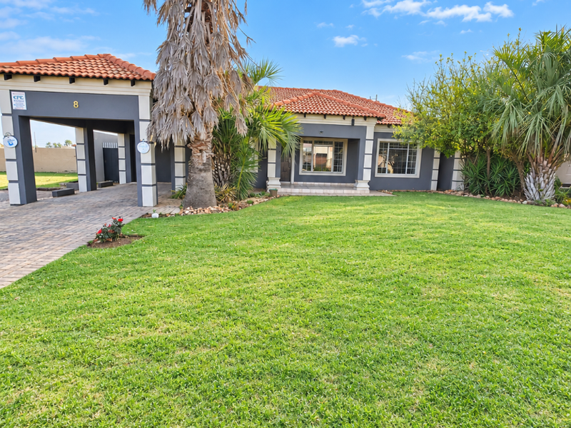 Front view of a well-maintained single-story house featuring a paved driveway, integrated carport, tiled roof, and a spacious front lawn.