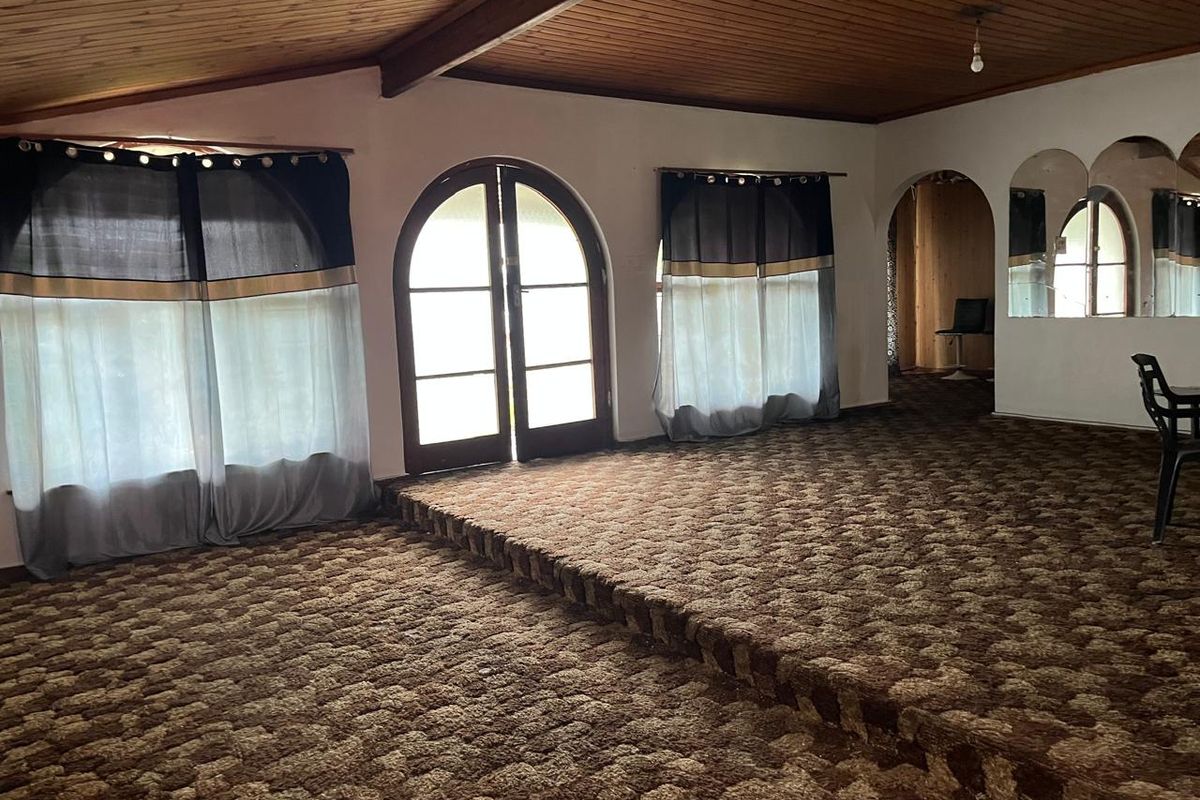 Spacious living area featuring a raised platform, timber-clad vaulted ceiling, and arched double doors leading to the exterior.