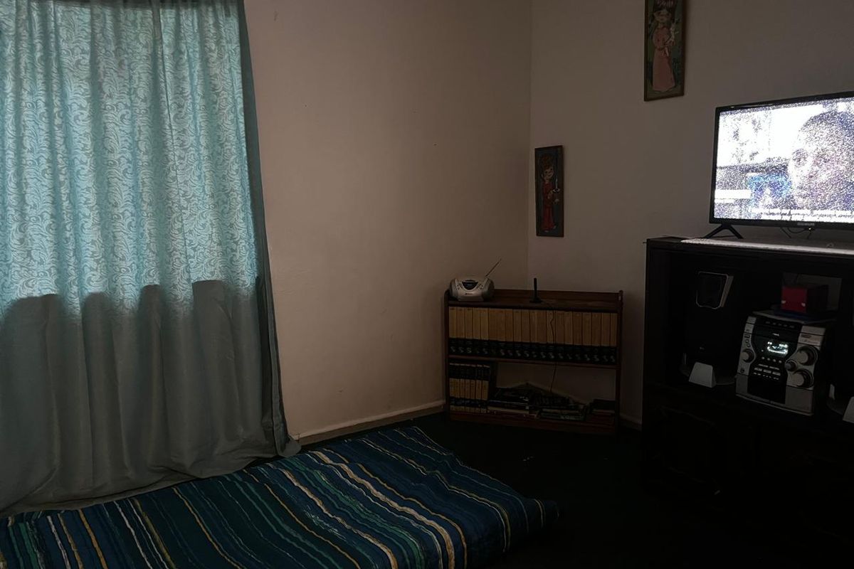 A simple bedroom space with basic finishes, featuring a window with curtains and dark flooring.