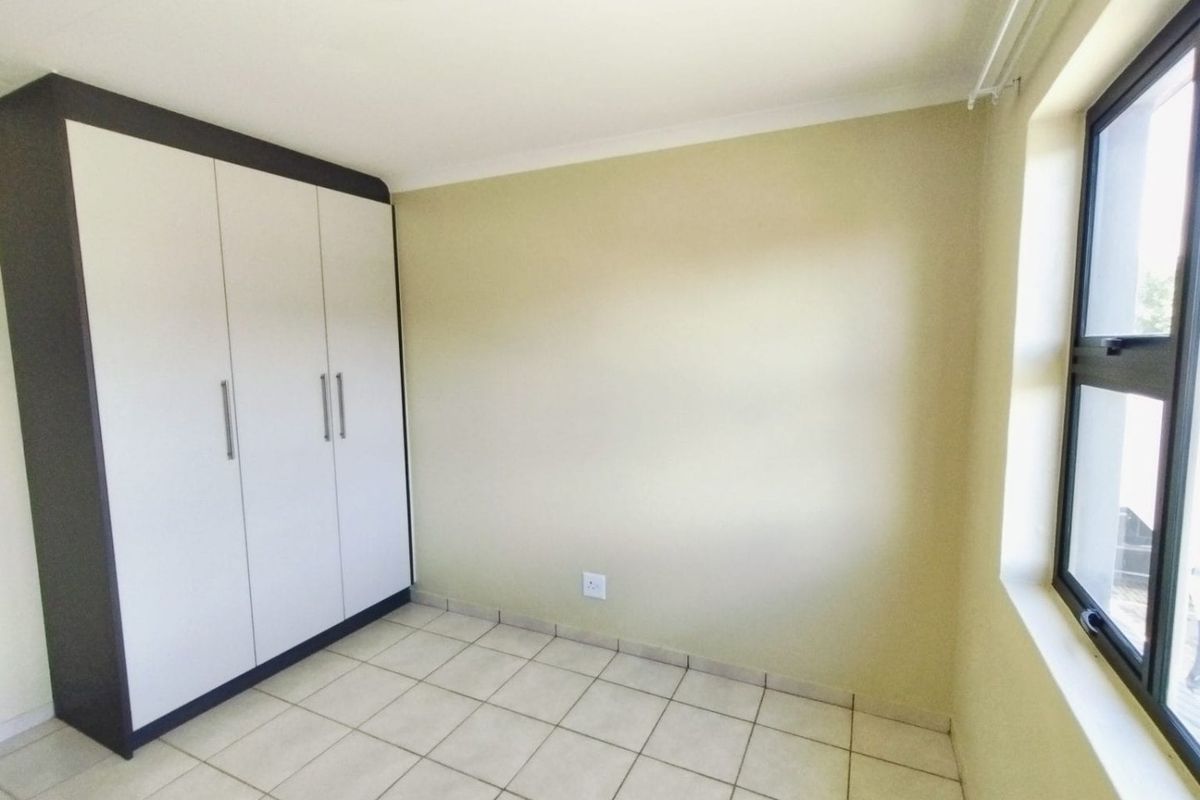 A clean, empty bedroom featuring neutral tiled flooring, built-in cupboards, and a large window providing natural light.