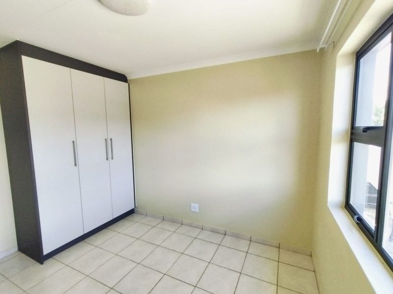 A clean, empty bedroom featuring neutral tiled flooring, built-in cupboards, and a large window providing natural light.
