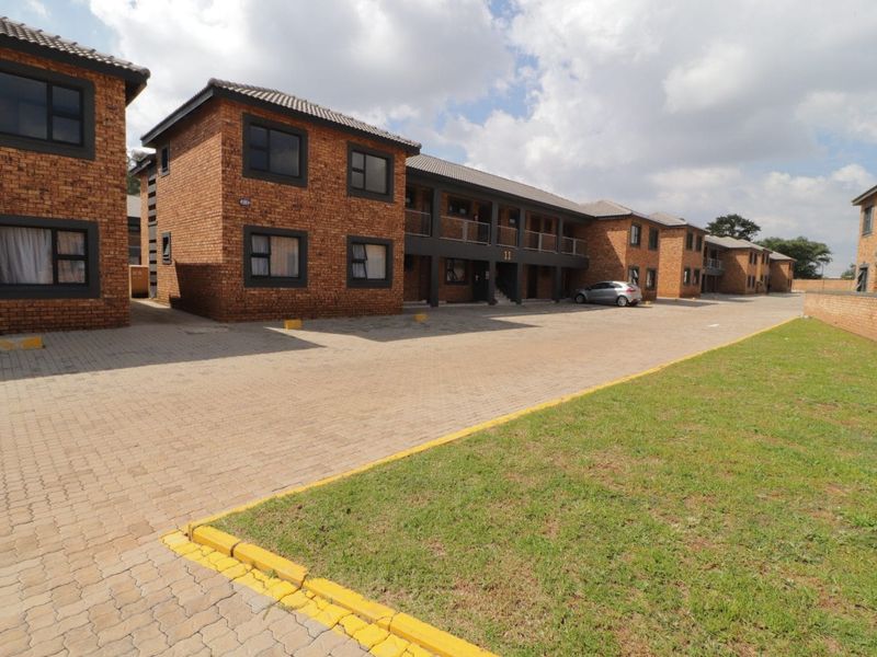 Exterior view of a multi-story face brick residential complex featuring paved driveway access and communal lawn areas.