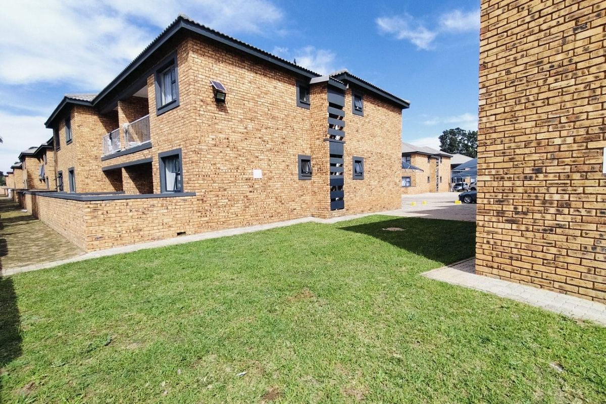 Exterior view of a multi-story face brick residential building featuring a lawn, paved pathways, and private balconies.