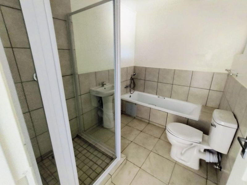 A functional bathroom featuring a pedestal basin, a separate shower enclosure, a bathtub, and a toilet with neutral ceramic tiling throughout.