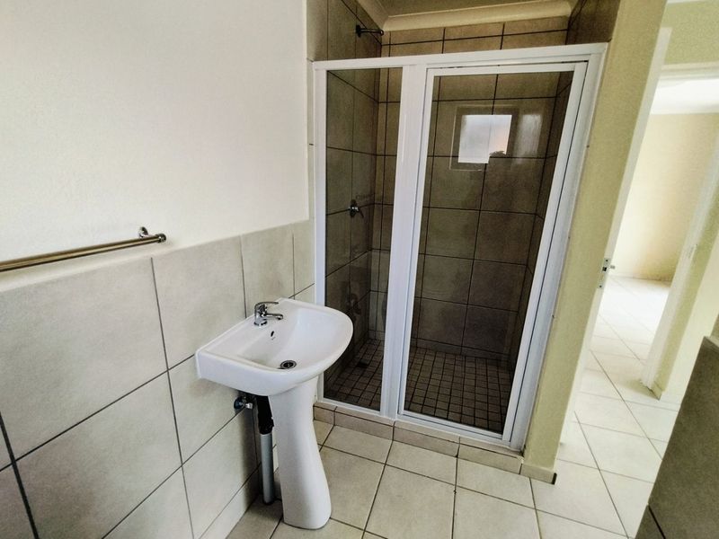 A functional bathroom featuring a pedestal basin, tiled flooring, and a glass-enclosed shower unit.