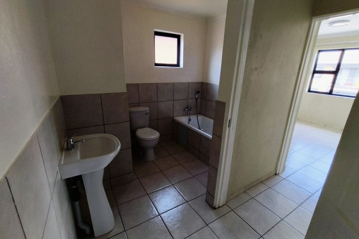 A functional bathroom featuring a pedestal basin, toilet, and bathtub with neutral tiled finishes, presenting a clean and well-maintained space.