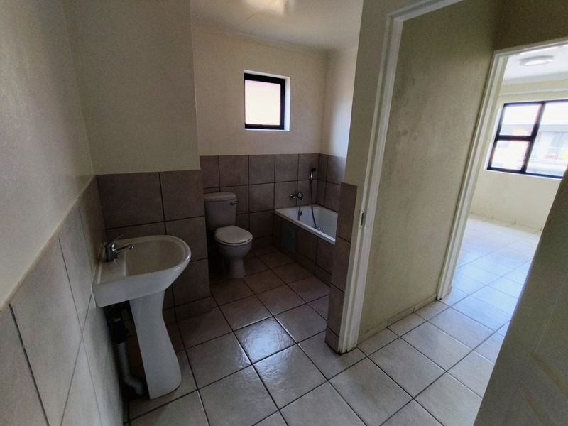 A functional bathroom featuring a pedestal basin, toilet, and bathtub with neutral tiled finishes, presenting a clean and well-maintained space.