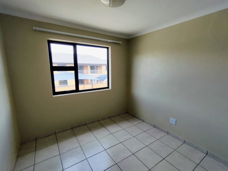 A clean, empty bedroom featuring neutral wall paint, tiled flooring, and an aluminium-framed window, providing a versatile space ready for furnishing.