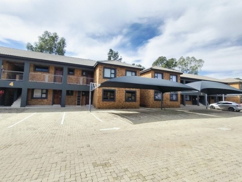 Front view of a multi-unit residential complex featuring face-brick construction, tiled roofing, and dedicated paved parking bays with shade cloth carports.