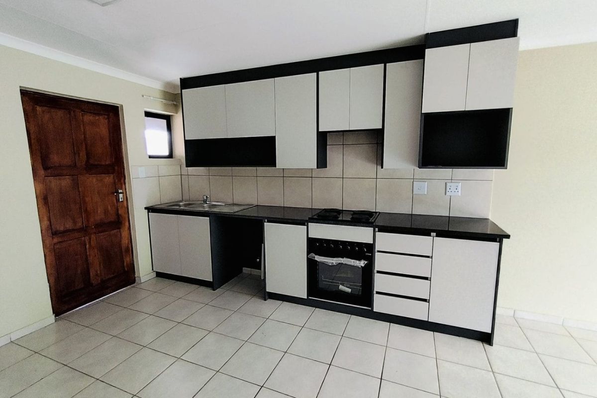 A clean, modern kitchen featuring two-tone cabinetry, built-in oven and hob, tiled flooring, and a tiled backsplash.