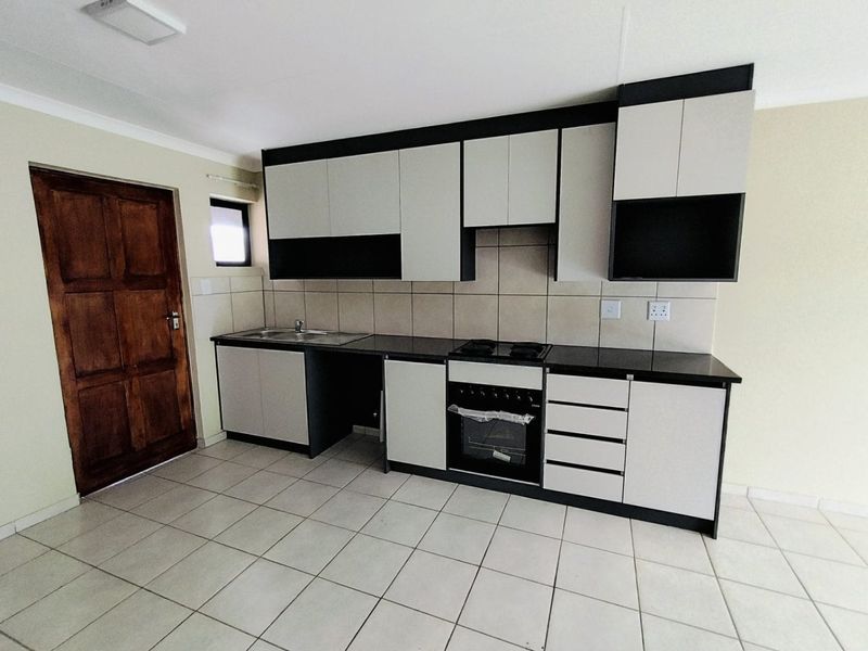 A clean, modern kitchen featuring two-tone cabinetry, built-in oven and hob, tiled flooring, and a tiled backsplash.