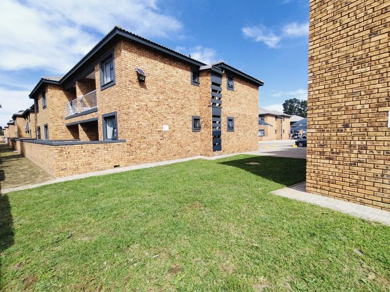 Exterior view of a multi-story face brick residential building featuring a lawn, paved pathways, and private balconies.