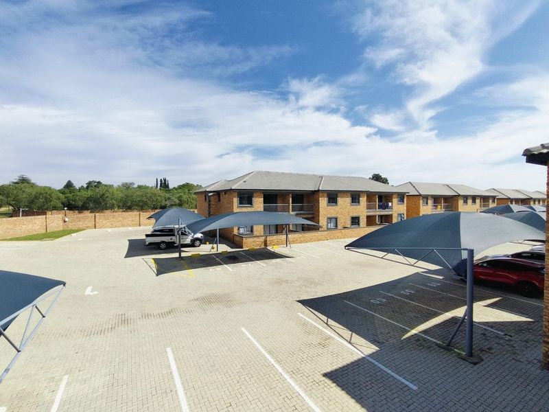An elevated view of a residential complex featuring a paved parking area with shade cloth carports and multi-story brick buildings with balconies.