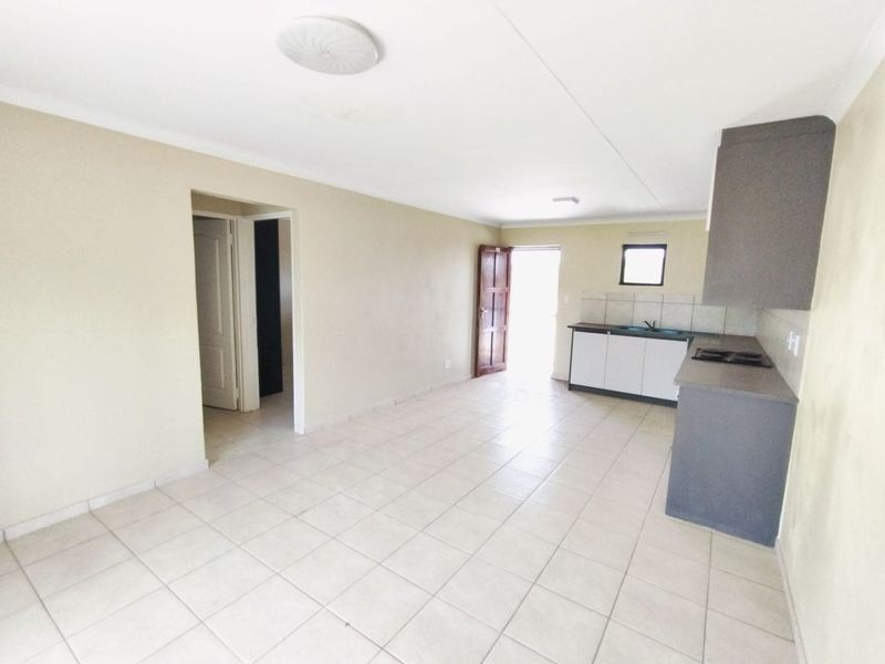 Open-plan living area featuring tiled flooring and a compact kitchen with built-in cabinetry, sink, and hob, offering a functional blank canvas.