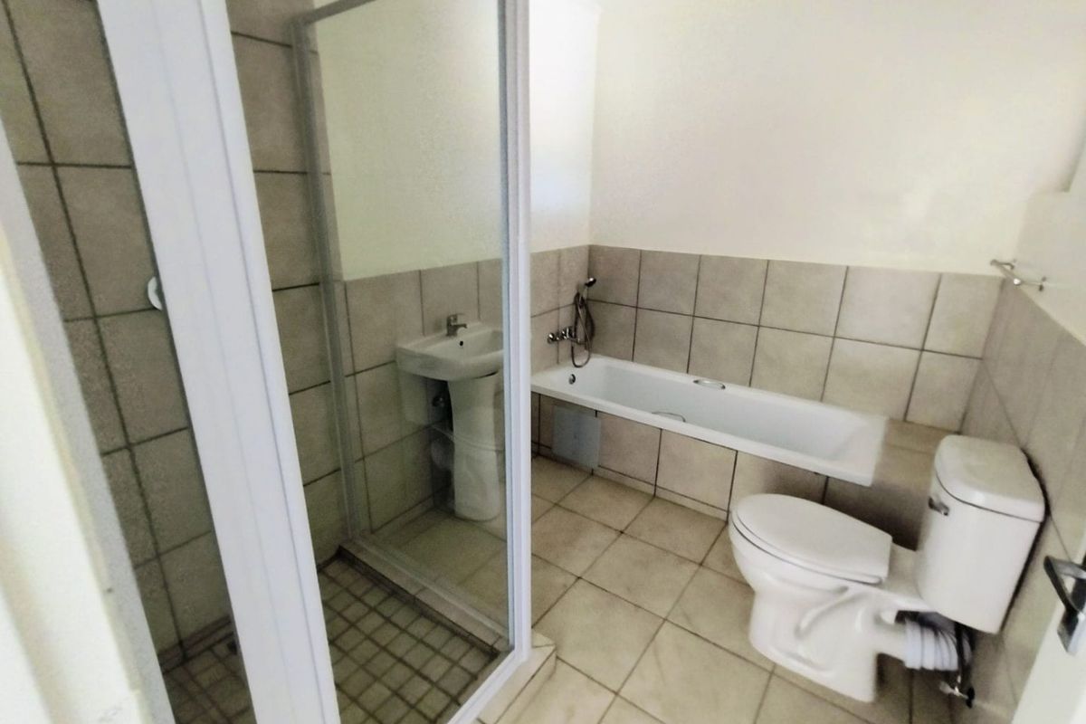 A functional bathroom featuring a pedestal basin, a separate shower enclosure, a bathtub, and a toilet with neutral ceramic tiling throughout.