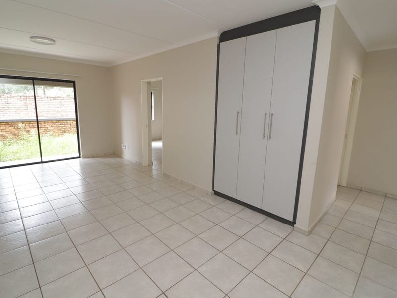A bright, empty bedroom featuring neutral tiled flooring, built-in cupboards, and a sliding glass door providing access to the exterior.