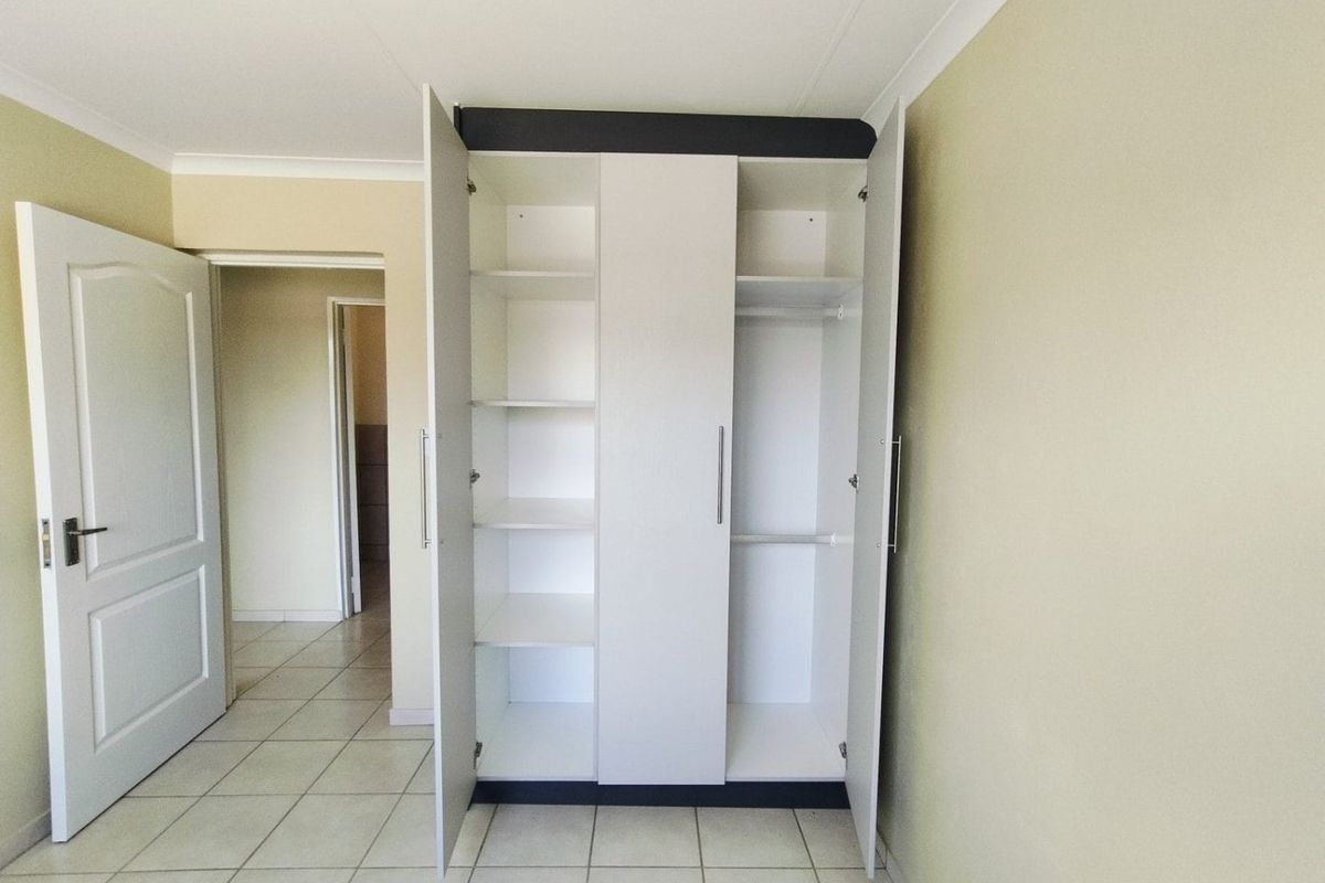 A clean, empty bedroom featuring neutral wall tones, tiled flooring, and a functional built-in wardrobe with shelving and hanging space.