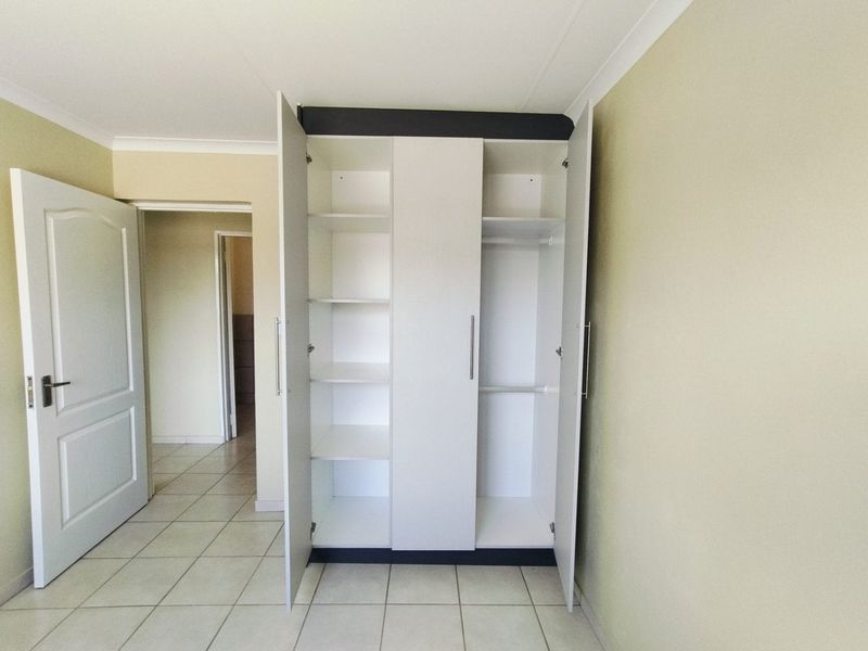 A clean, empty bedroom featuring neutral wall tones, tiled flooring, and a functional built-in wardrobe with shelving and hanging space.