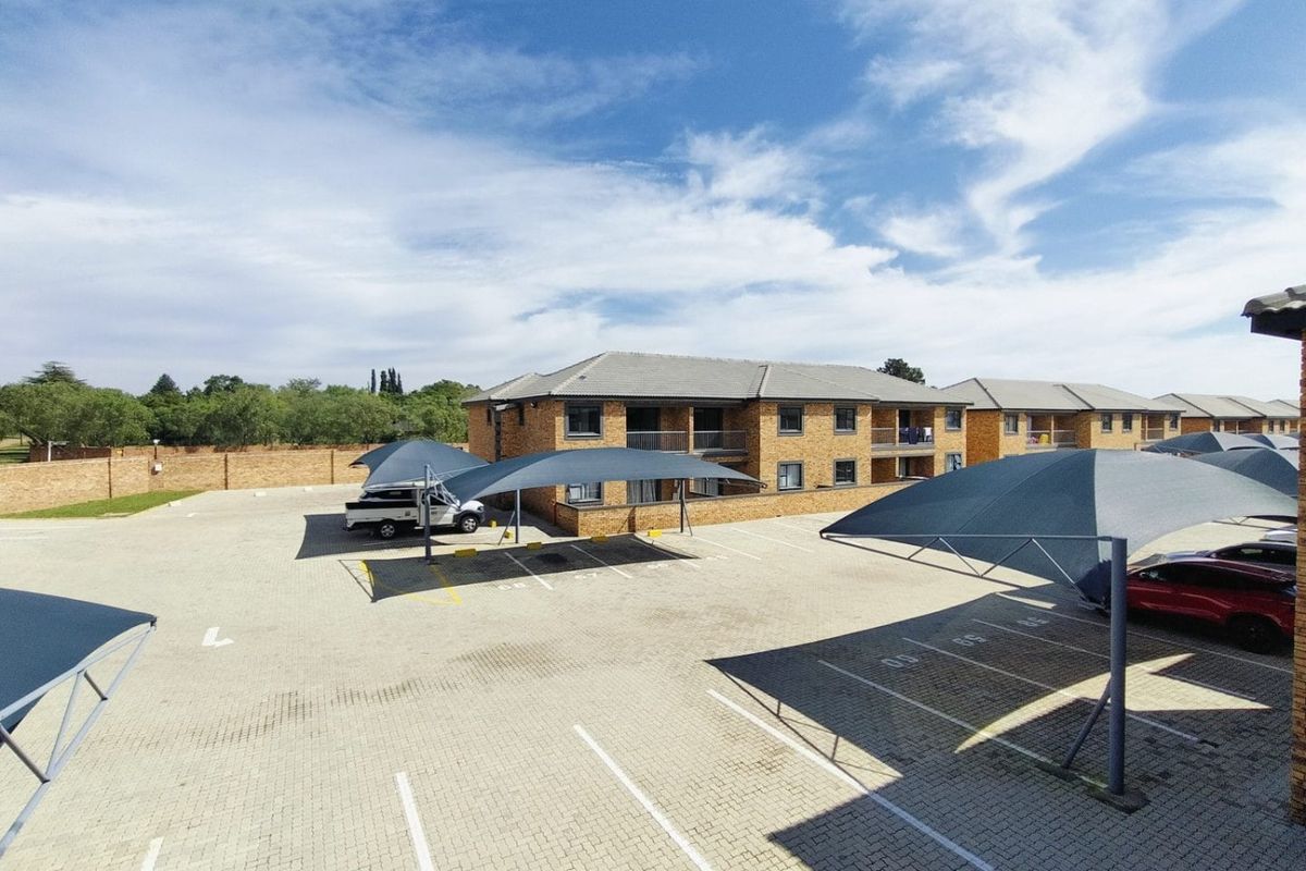 An elevated view of a residential complex featuring a paved parking area with shade cloth carports and multi-story brick buildings with balconies.